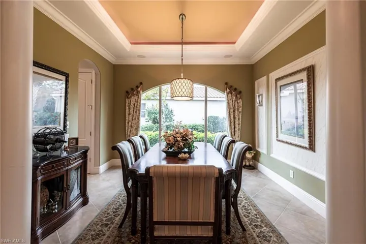 Dining room featuring arched walkways, crown molding, light tile patterned flooring, and a raised ceiling