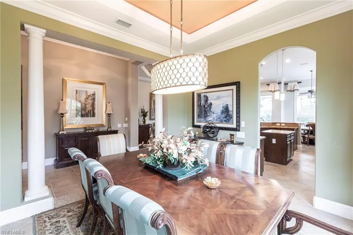 Dining area featuring arched walkways, crown molding, decorative columns, a tray ceiling, and light tile patterned floors