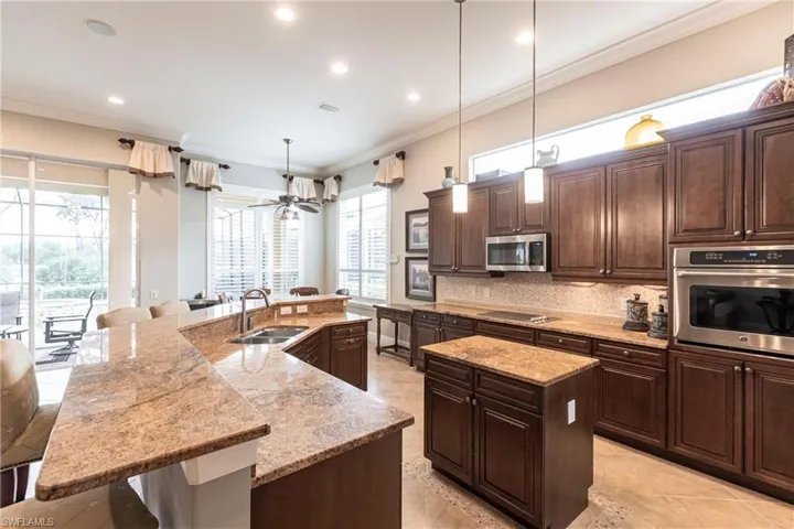 Kitchen with appliances with stainless steel finishes, dark brown cabinets, a kitchen bar, decorative light fixtures, and ornamental molding