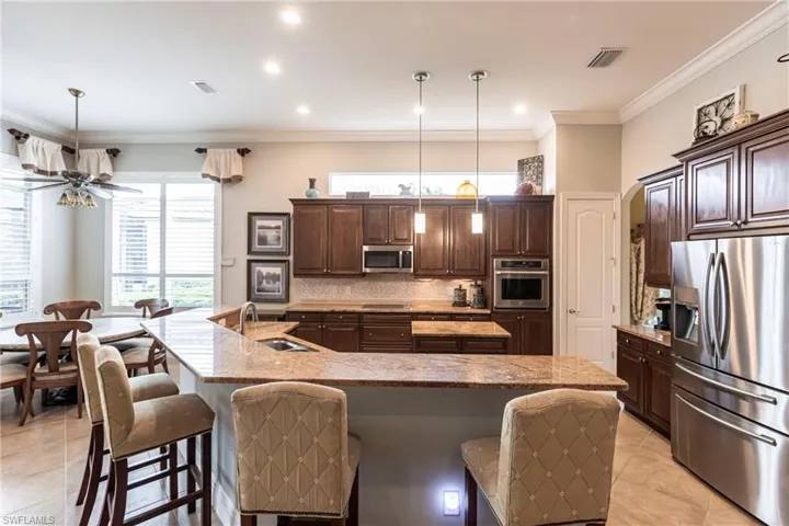Kitchen with stainless steel appliances, dark brown cabinets, a large island with sink, light tile patterned flooring, and a kitchen breakfast bar