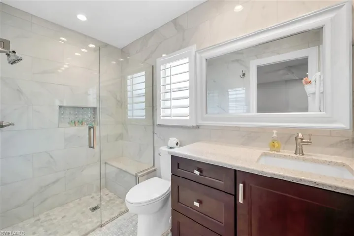 Full bath with a stall shower, toilet, tile walls, and vanity