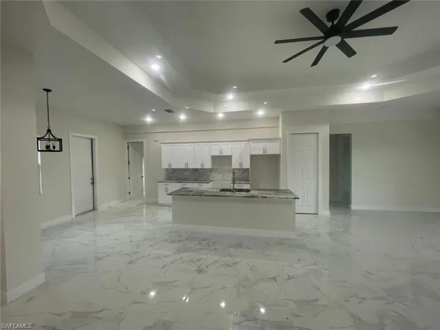 Unfurnished living room featuring a raised ceiling, ceiling fan, and light tile floors