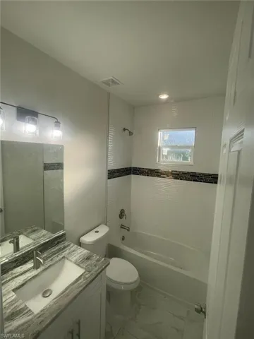 Full bathroom with tile flooring, tiled shower / bath, oversized vanity, and toilet