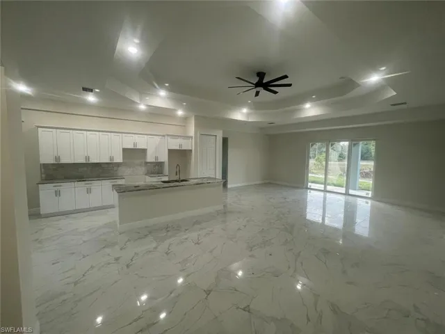 Kitchen with backsplash, a center island with sink, ceiling fan, a tray ceiling, and light tile floors