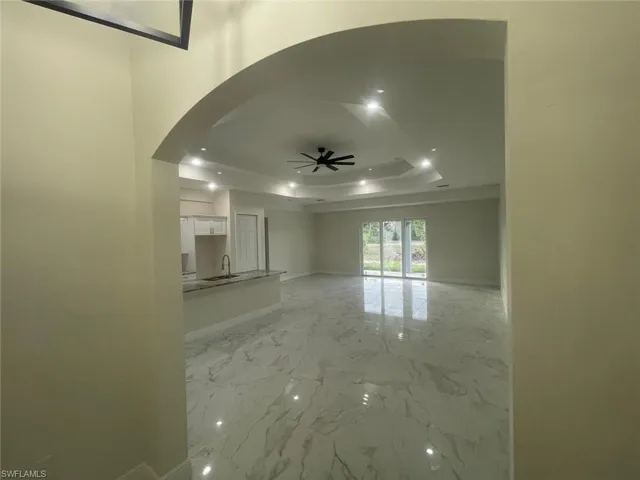 Unfurnished living room featuring light tile floors, sink, ceiling fan, and a raised ceiling
