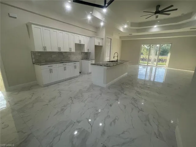 Kitchen with a raised ceiling, a kitchen island with sink, white cabinetry, and light tile floors