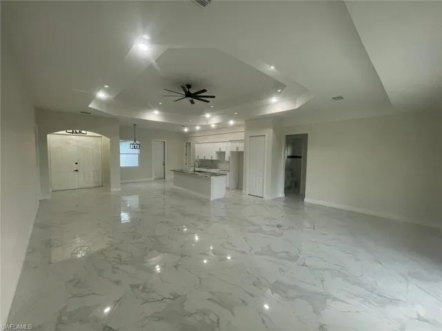 Unfurnished living room with ceiling fan, a raised ceiling, and light tile flooring