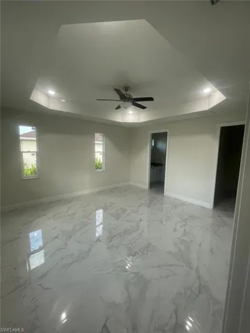 Unfurnished room featuring light tile floors, ceiling fan, and a raised ceiling