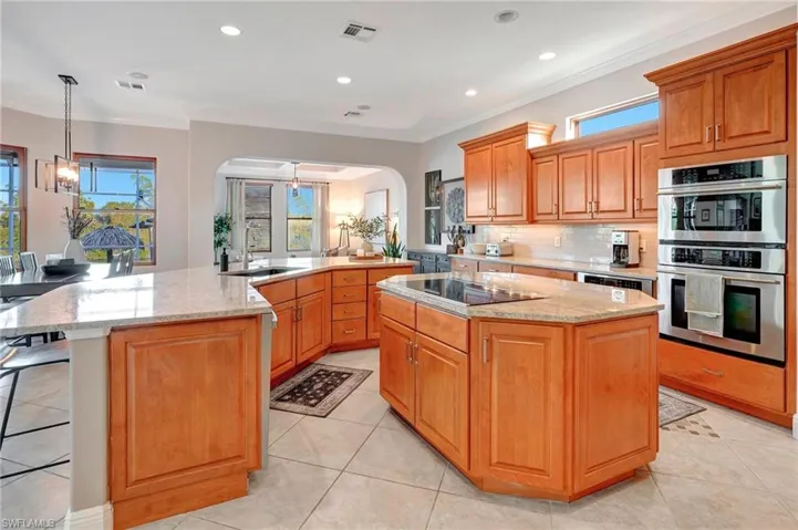 Kitchen featuring a spacious island, light stone counters, pendant lighting, stainless steel double oven, and black electric stovetop