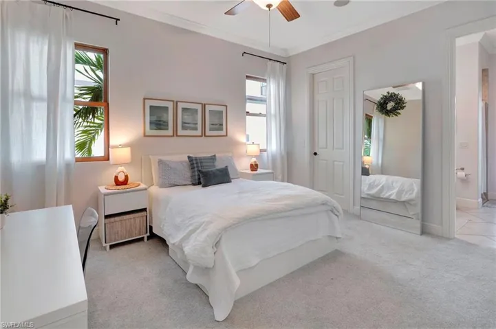 Carpeted bedroom with ensuite bath, ornamental molding, and ceiling fan