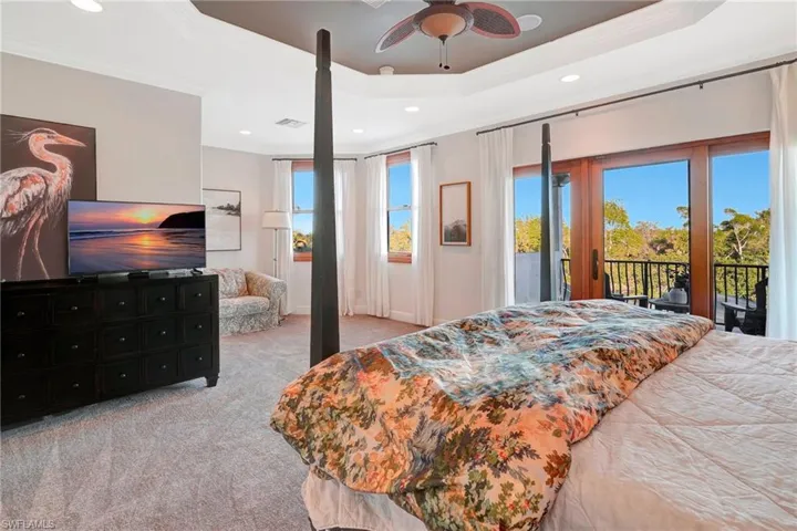 Bedroom with light carpet, ornamental molding, a raised ceiling, ceiling fan, and access to exterior