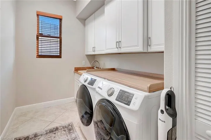 Washroom with cabinets, light tile patterned flooring, washer and dryer, and sink