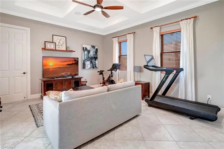 Exercise area with coffered ceiling, light tile patterned floors, ornamental molding, and ceiling fan