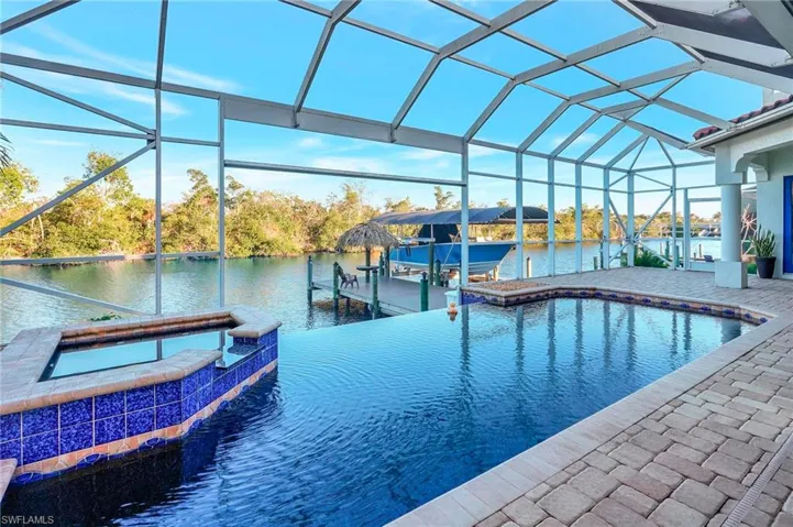 View of swimming pool featuring an in ground hot tub, a water view, a lanai, and a dock