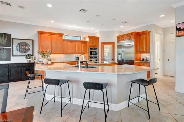 Kitchen with sink, a kitchen bar, a large island with sink, stainless steel appliances, and light stone countertops