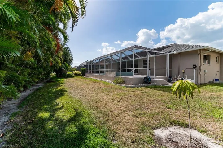 Rear view of house with a lawn, stucco siding, and a lanai