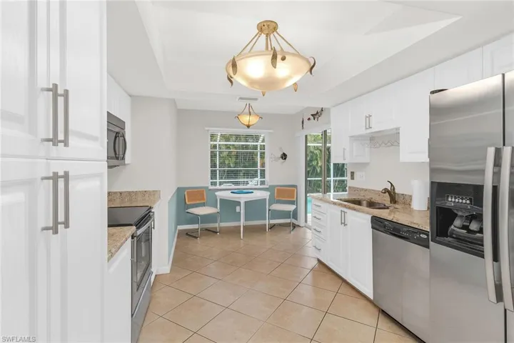 Kitchen featuring stainless steel appliances, white cabinets, a sink, light tile patterned flooring, and a tray ceiling