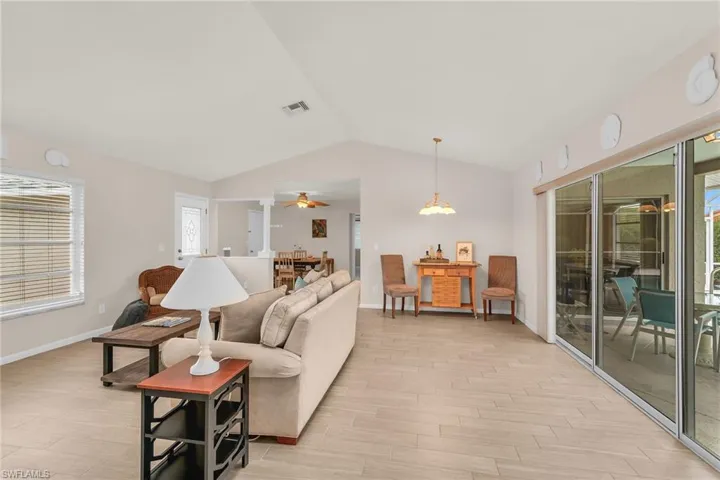 Living area with visible vents, ceiling fan, light wood-style floors, baseboards, and vaulted ceiling