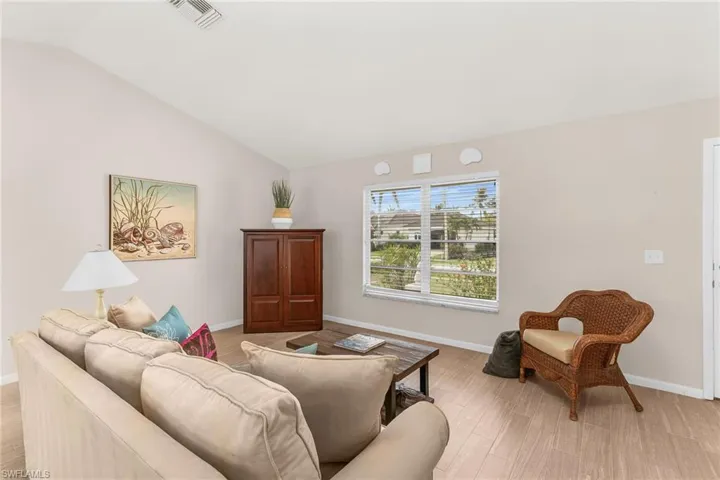 Living room with light wood-style flooring, visible vents, vaulted ceiling, and baseboards