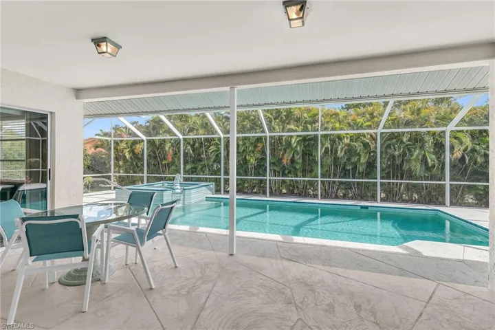 View of pool featuring glass enclosure, a pool with connected hot tub, and a patio area