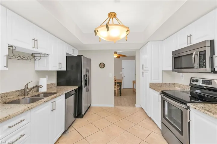 Kitchen featuring light tile patterned floors, white cabinetry, a sink, appliances with stainless steel finishes, and a raised ceiling