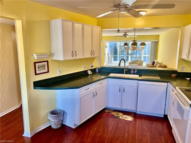 Kitchen featuring dark wood-type flooring, sink, kitchen peninsula, white appliances, and white cabinets