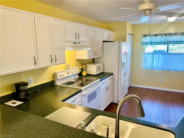 Kitchen with sink, white appliances, ceiling fan, white cabinetry, and dark hardwood / wood-style flooring