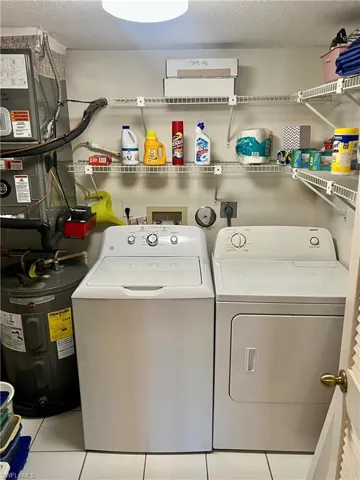 Laundry area featuring water heater, light tile patterned flooring, washing machine and clothes dryer, and a textured ceiling