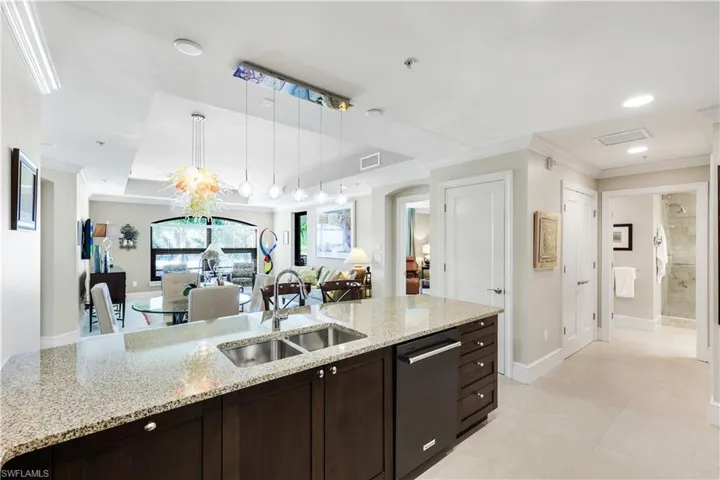 Kitchen featuring dark brown cabinetry, ornamental molding, light stone countertops, stainless steel dishwasher, and pendant lighting