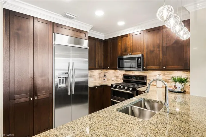 Kitchen featuring appliances with stainless steel finishes, light stone countertops, dark brown cabinets, backsplash, and hanging light fixtures