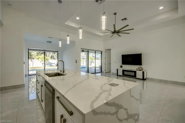 Kitchen with sink, decorative light fixtures, a raised ceiling, an island with sink, and white cabinets