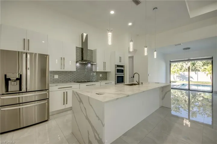 Kitchen featuring white cabinetry, wall chimney range hood, stainless steel appliances, and an island with sink