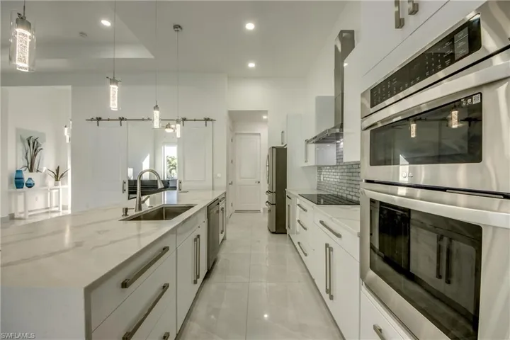 Kitchen featuring white cabinetry, hanging light fixtures, stainless steel appliances, a barn door, and wall chimney exhaust hood
