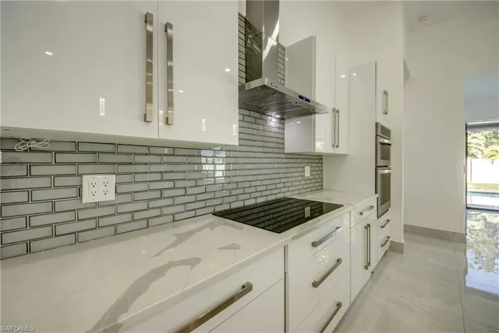 Kitchen with white cabinetry, light stone countertops, wall chimney range hood, and black electric cooktop