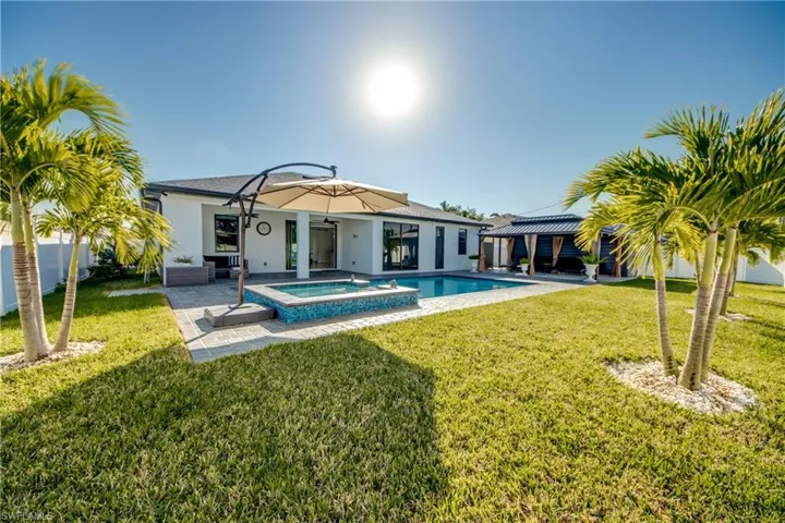 Back of property featuring a pool with hot tub, a yard, and a patio