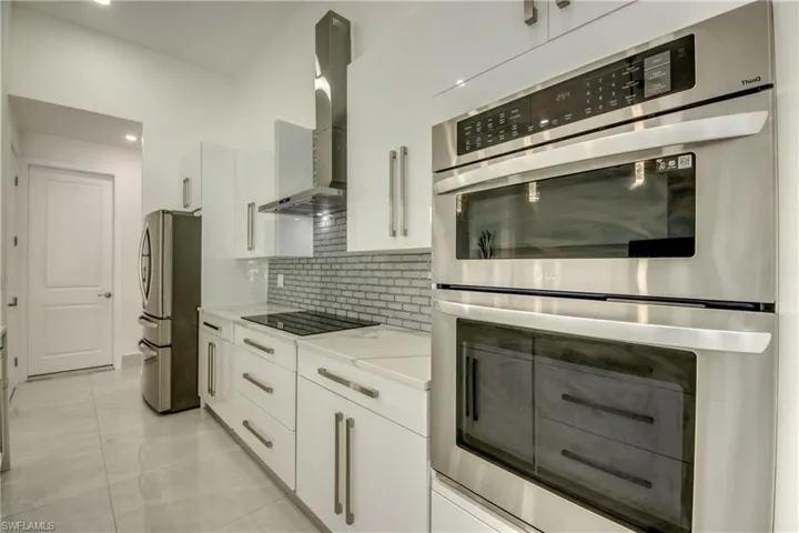Kitchen featuring wall chimney range hood, light stone countertops, white cabinets, and appliances with stainless steel finishes