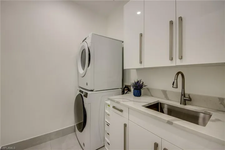 Washroom with cabinets, stacked washer / drying machine, sink, and light tile patterned floors