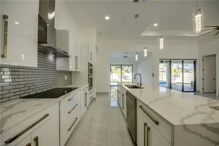 Kitchen featuring wall chimney exhaust hood, sink, hanging light fixtures, and white cabinets