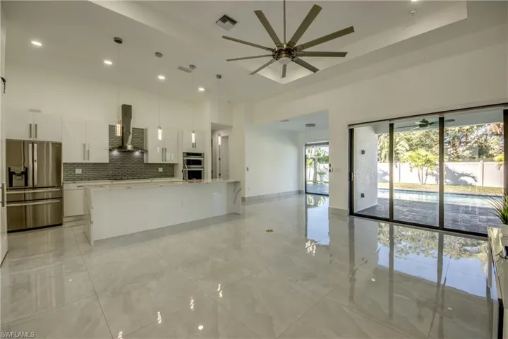 Kitchen featuring wall chimney range hood, white cabinetry, hanging light fixtures, stainless steel appliances, and a center island with sink