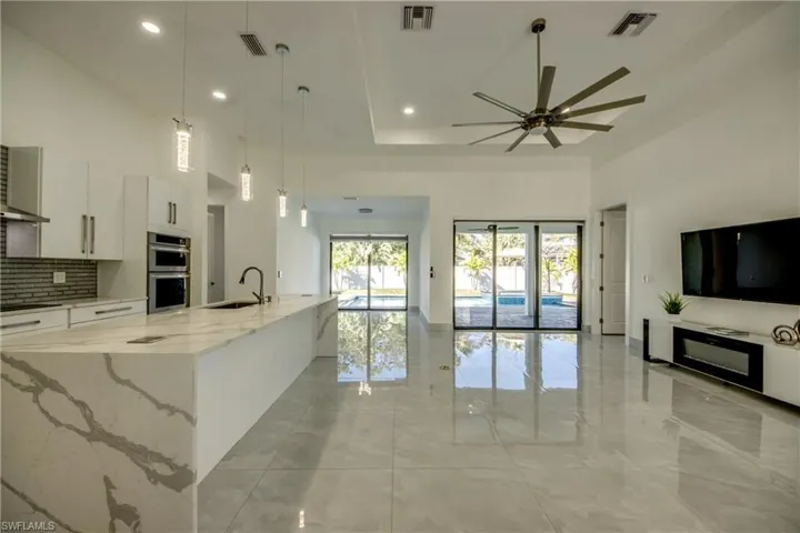 Kitchen featuring pendant lighting, sink, a large island, light stone countertops, and white cabinets