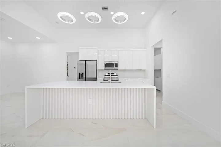 Modern kitchen featuring a large waterfall island with ribbed paneling, high ceilings, recessed lighting, and three contemporary circular chandeliers