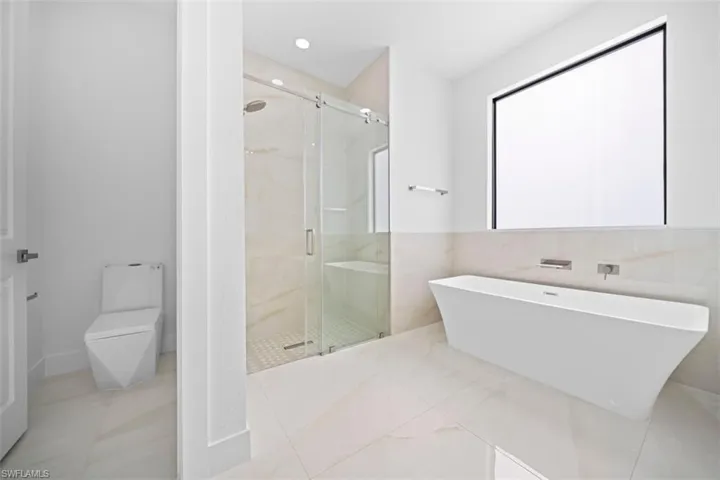 Bathroom featuring a freestanding soaking tub, a large walk-in shower with a glass enclosure, light-toned tile flooring, and a contemporary window