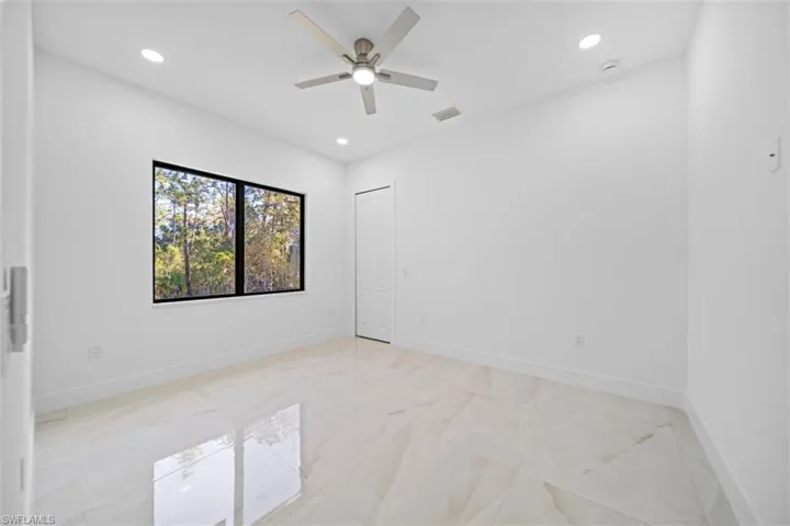 Spacious room featuring large format polished porcelain tile flooring, a modern ceiling fan with integrated lighting, recessed ceiling lights, and a window with black trim