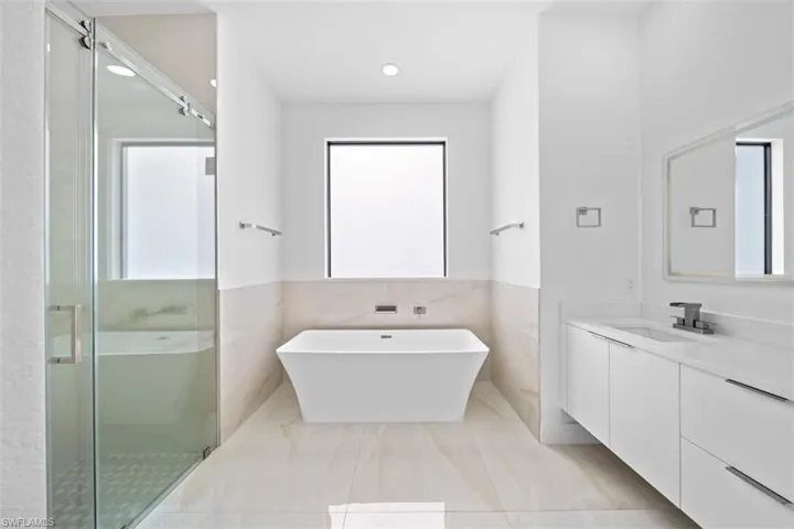 Freestanding soaking tub with a large window, complemented by a glass-enclosed shower with a rain showerhead