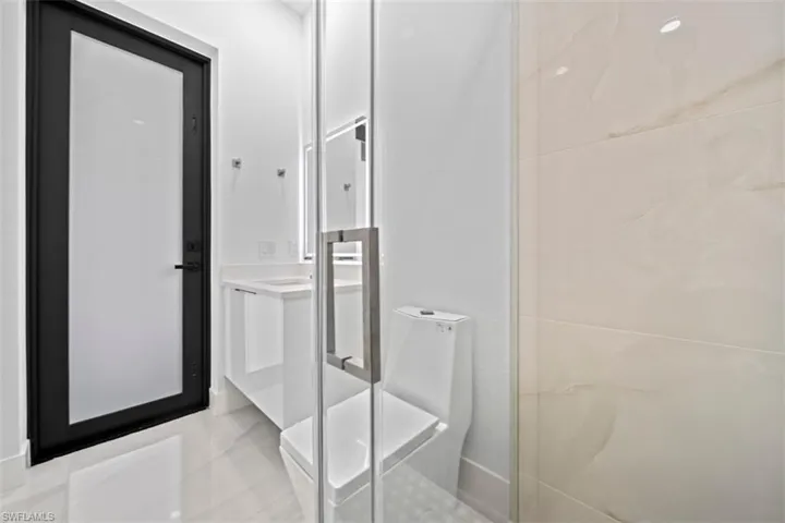 Contemporary bathroom featuring a frameless glass shower enclosure, white vanity with integrated sink, and large format floor tiling