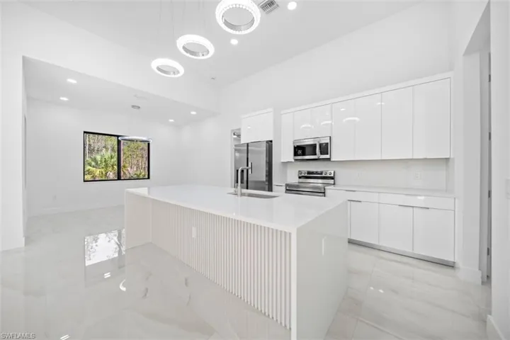 Contemporary kitchen featuring a large center island with a waterfall countertop, white high-gloss cabinetry, stainless steel appliances, and a tile backsplash