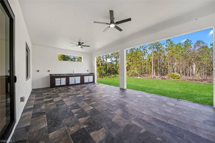 Expansive outdoor living area featuring slate-look tile flooring and a built-in outdoor kitchen with integrated sink