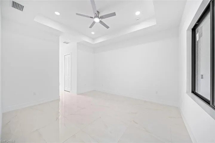 Bright interior space featuring large format tile flooring, a tray ceiling with recessed lighting, and a ceiling fan