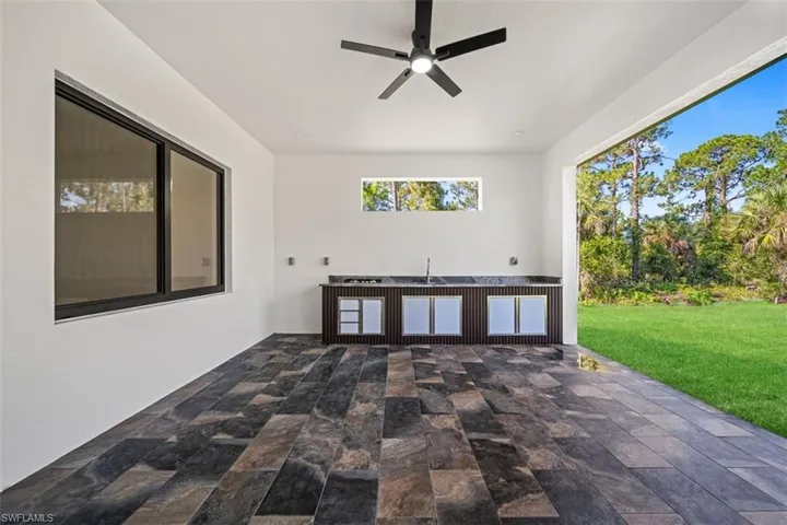 Expansive covered patio featuring large-format tile flooring, a built-in outdoor kitchen with integrated sink and under-counter refrigeration, a ceiling fan, and a wide-open exterior connection to the backyard