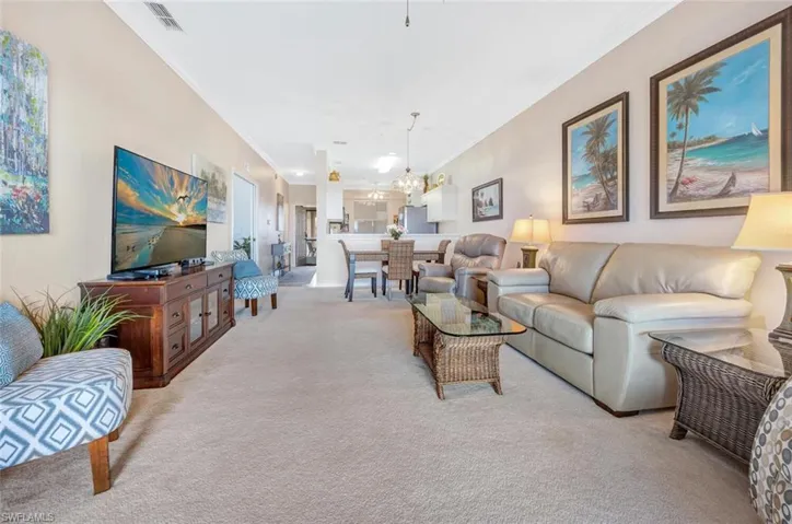 Living area featuring carpet floors, ornamental molding, visible vents, and an inviting chandelier